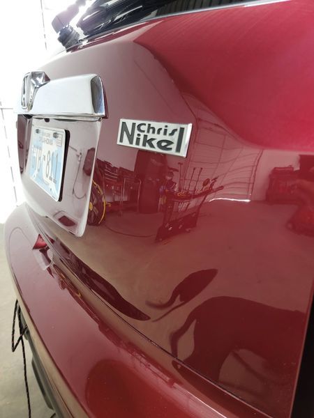 Red car with a license plate and a chrome badge that reads 