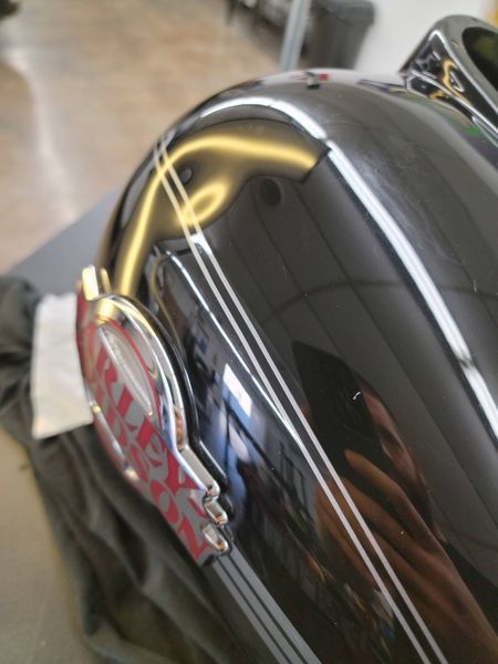 Close-up of a black motorcycle gas tank with white pinstripes and a chrome emblem.