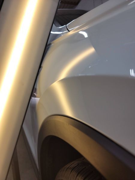 White car's fender with a dent being assessed using a light and reflection to identify the damage.