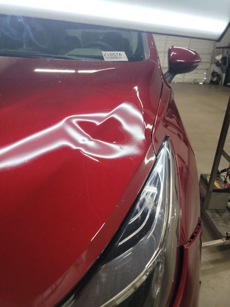 Red car hood with a significant dent, under repair lights.