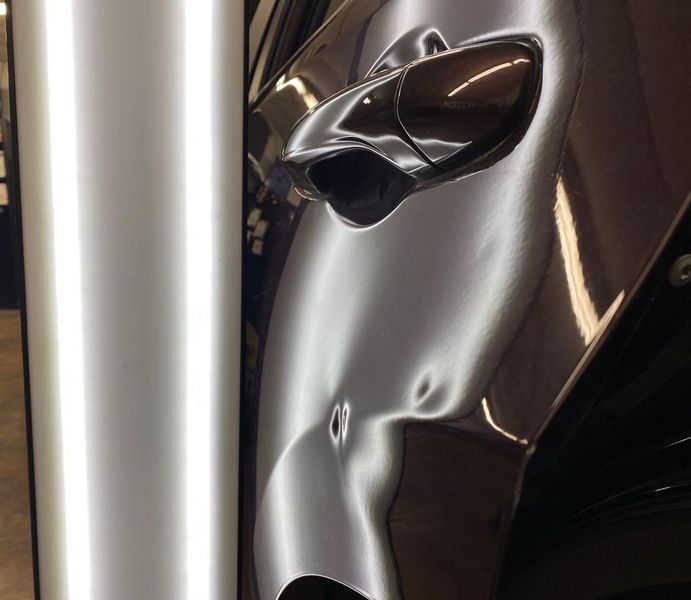 Car door with multiple dents reflecting white light.