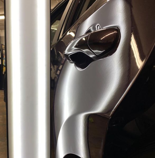 Car door with a dent being assessed with a light.