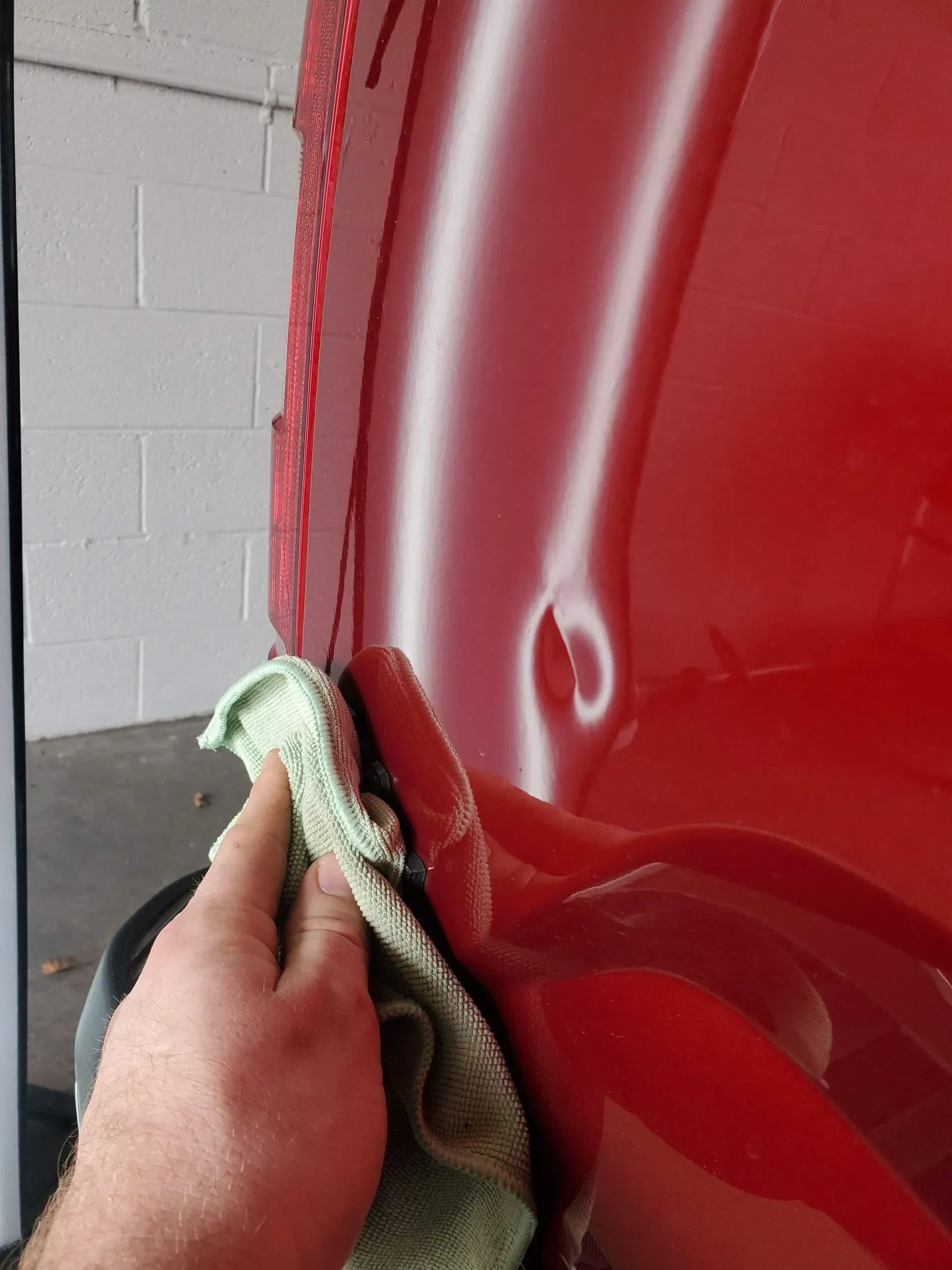 Hand wiping a dented red car panel with a green cloth.