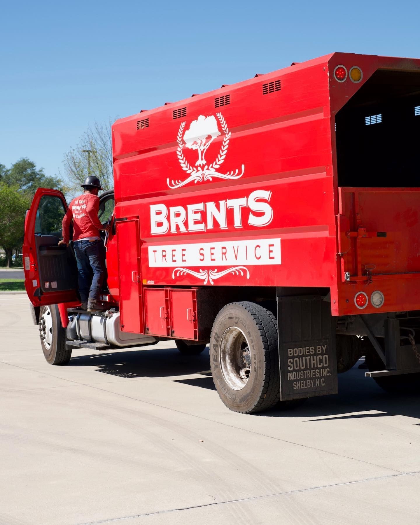 Red Brent's Tree Service truck with a person entering. Logos on side and back.