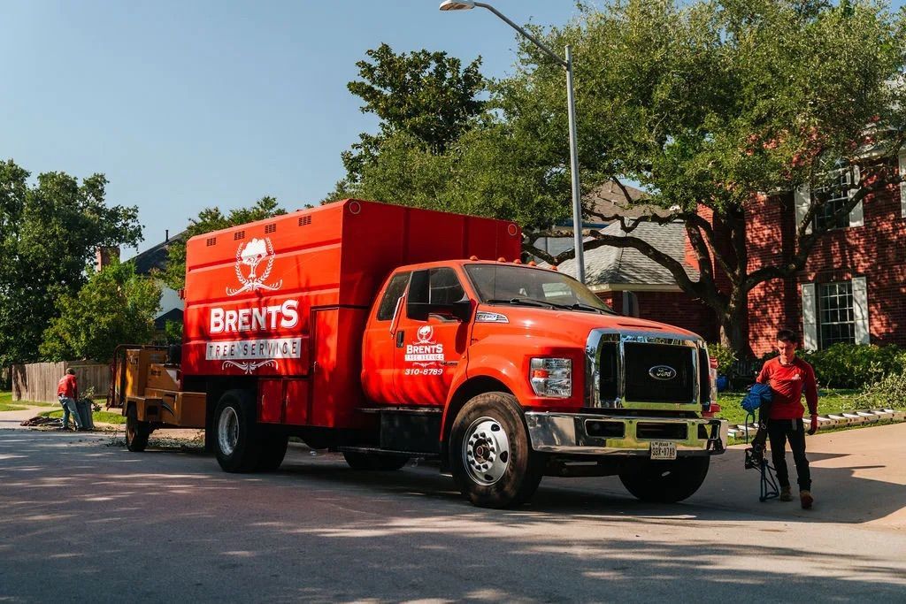 A bright red Brent's Tree Service truck parked on a residential street with a person standing nearby.