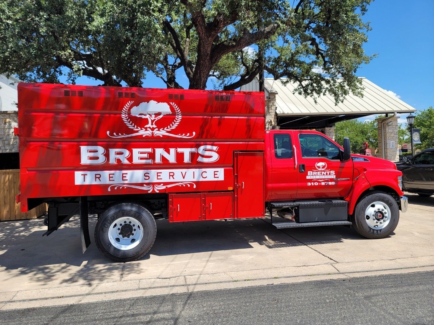 A bright red Brents Tree Service bucket truck parked on a sunny day.