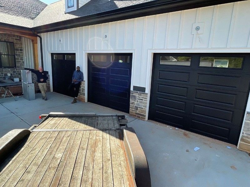 Driveway with a black garage door, blue door, and a person standing near the entrance.