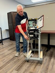 Man adjusting a wheeled metal machine cart in a room with tables and cabinets