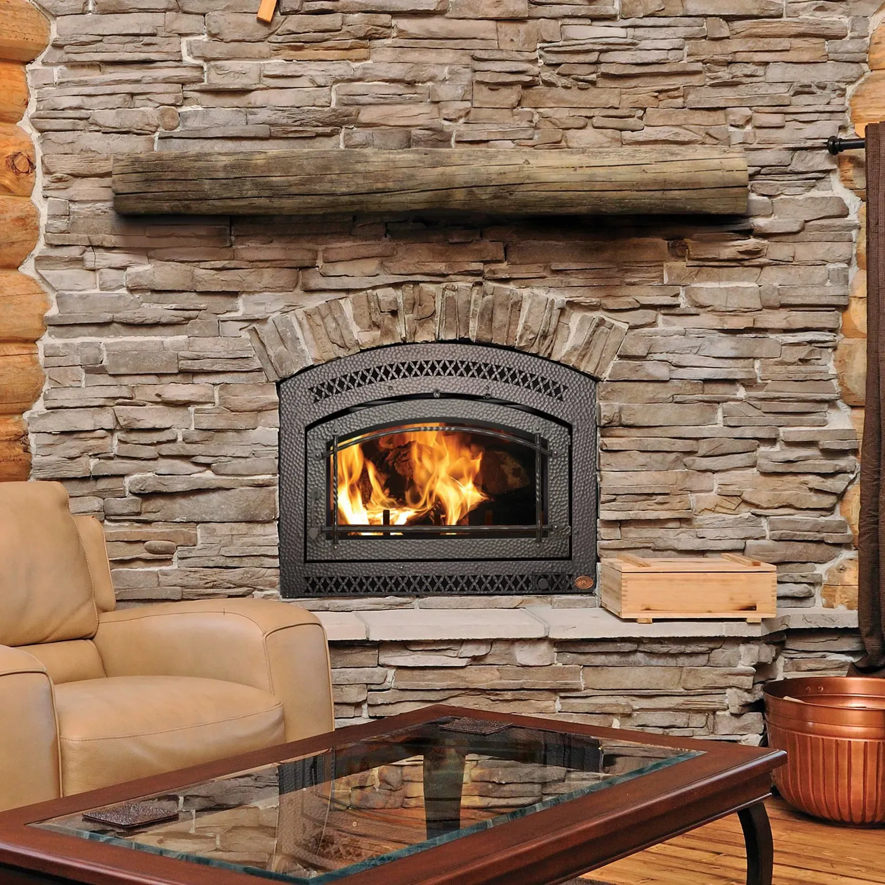 Fireplace with lit flames, stone surround, wooden beam mantel, leather couch, and glass-top coffee table.