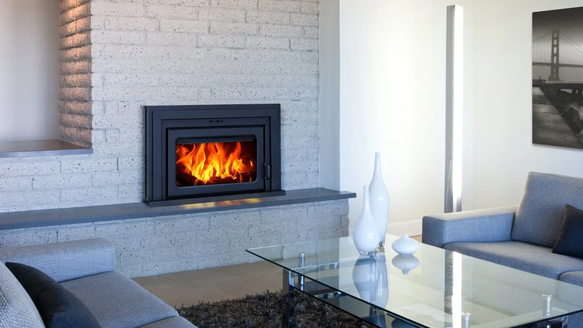 Fireplace with burning flames, set in a gray brick wall. Modern living room with couch, coffee table, and decor.