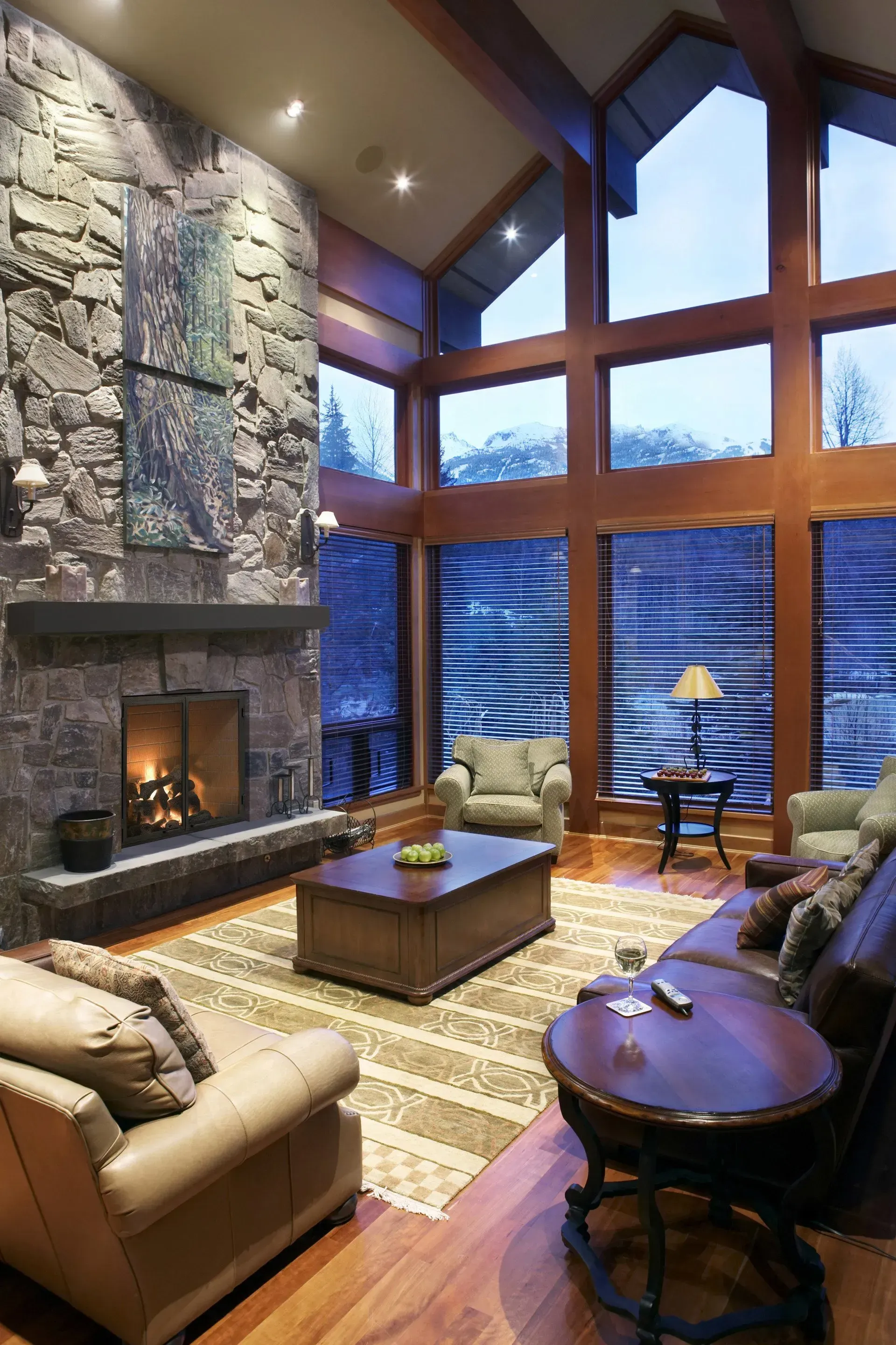 Living room with stone fireplace, large windows, and wood beams. Furnished with leather seating and a coffee table.
