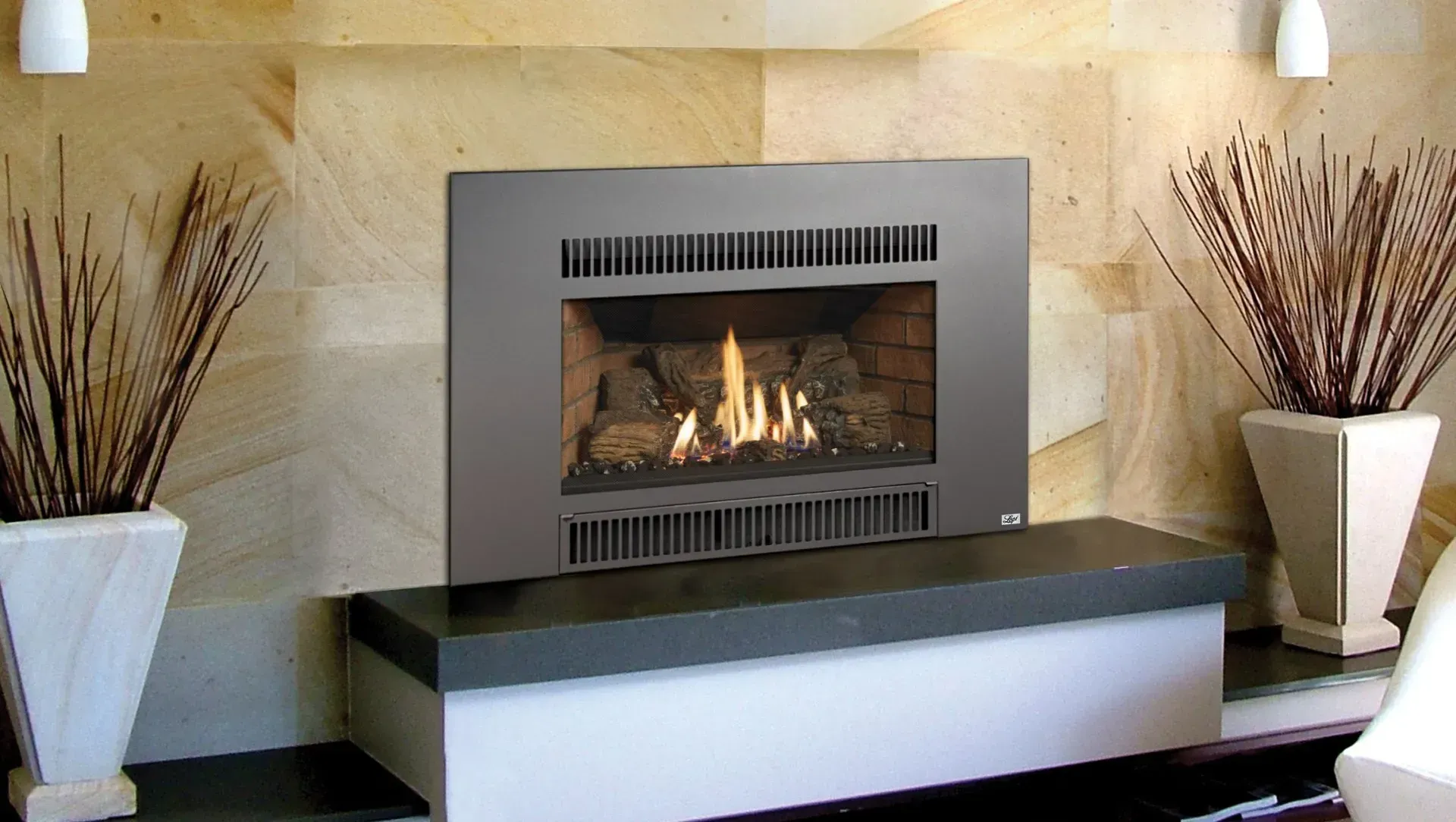 Modern gas fireplace with flames, flanked by decorative plants in white vases, set against a textured stone wall.