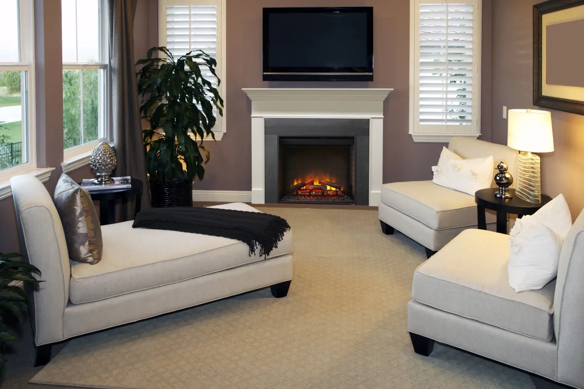 Living room with a fireplace, two chaise lounges, and a TV above the mantel, beige and purple tones.