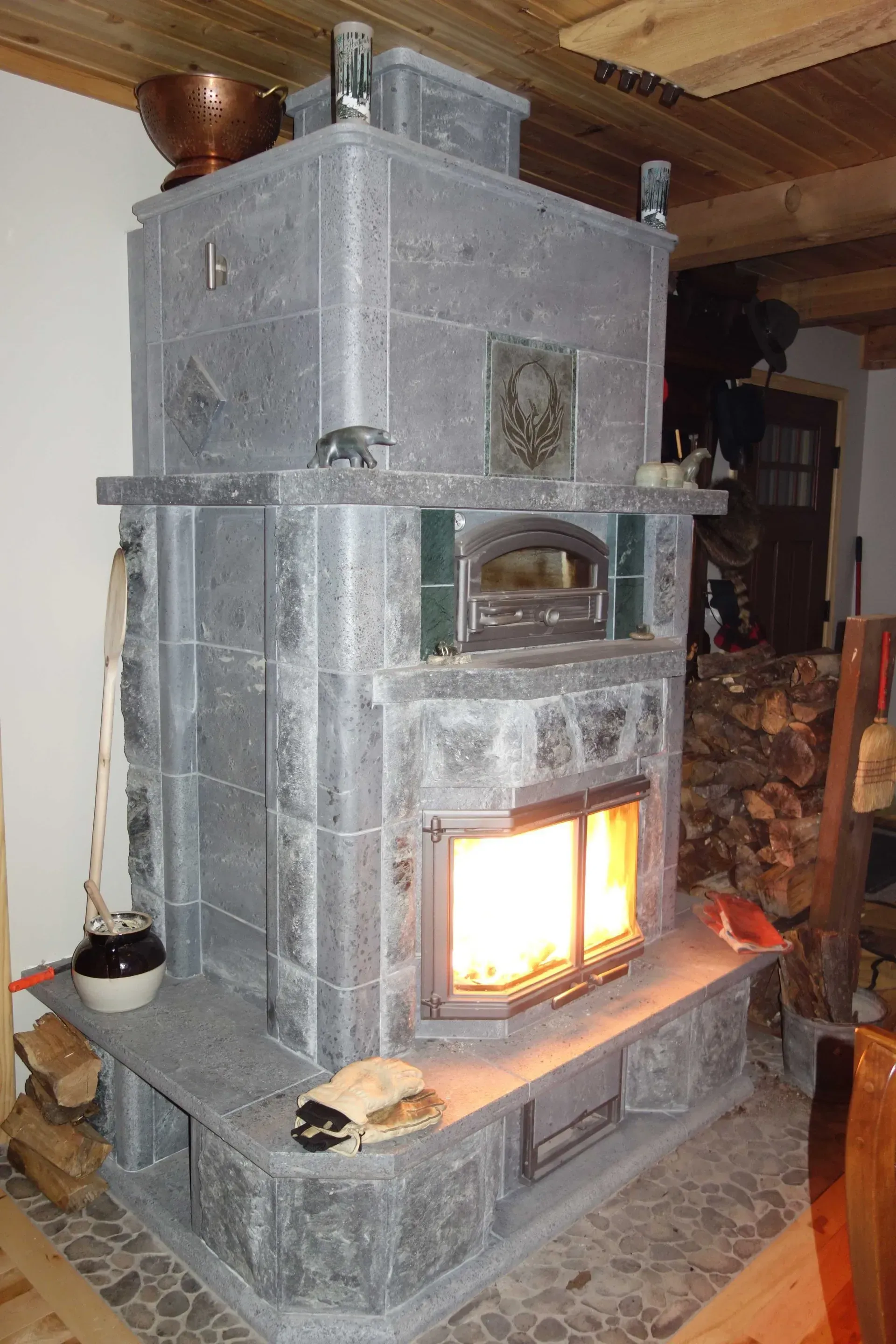Gray stone fireplace with a burning fire, oven, and chimney in a rustic interior.