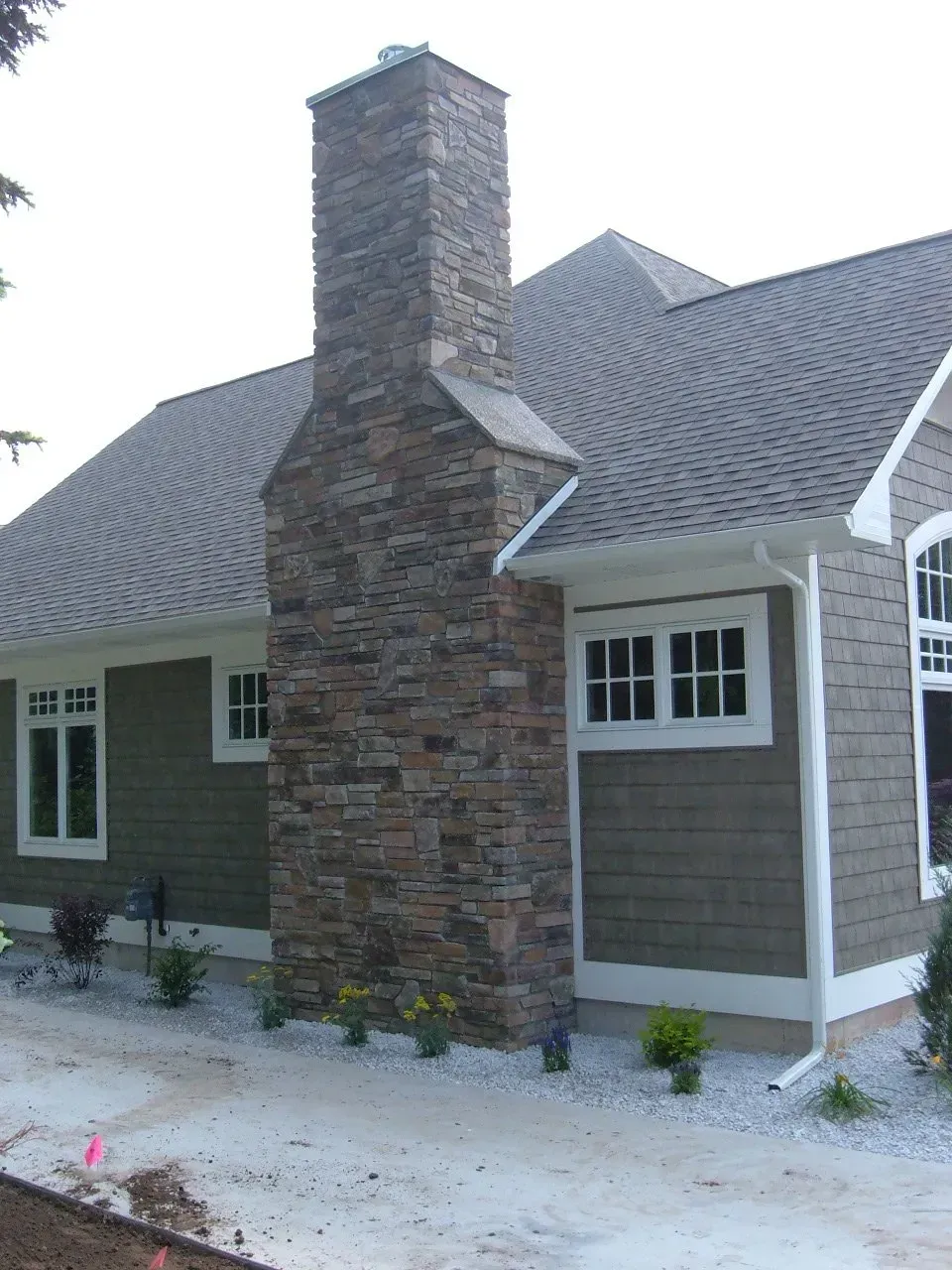 Stone chimney on a house with gray roof and green siding, white trim.