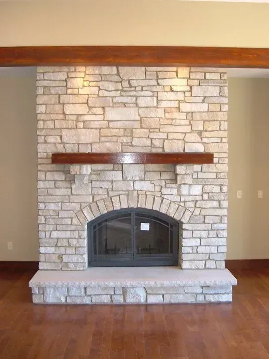 Stone fireplace with arched firebox, wooden mantel, set against beige walls, and hardwood floors.