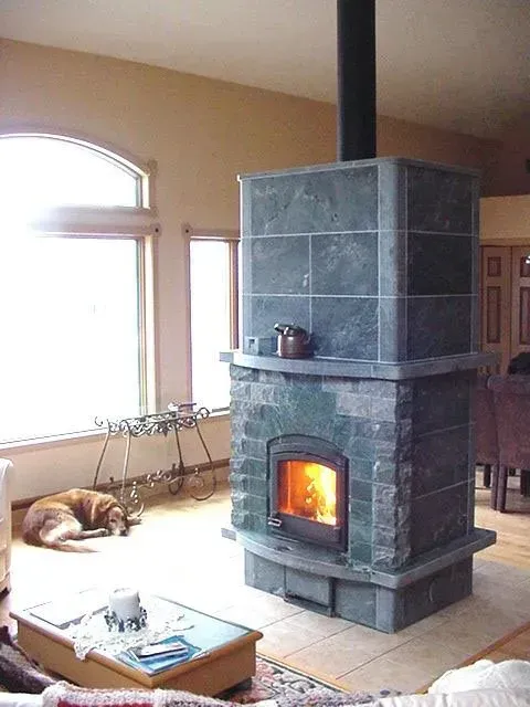 A tall, green stone fireplace with a burning fire, in a living room with a sleeping dog.