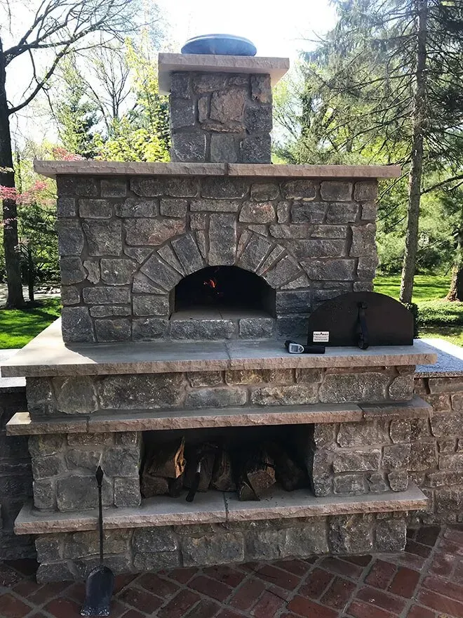 Stone outdoor pizza oven with fire burning inside and wood storage below.