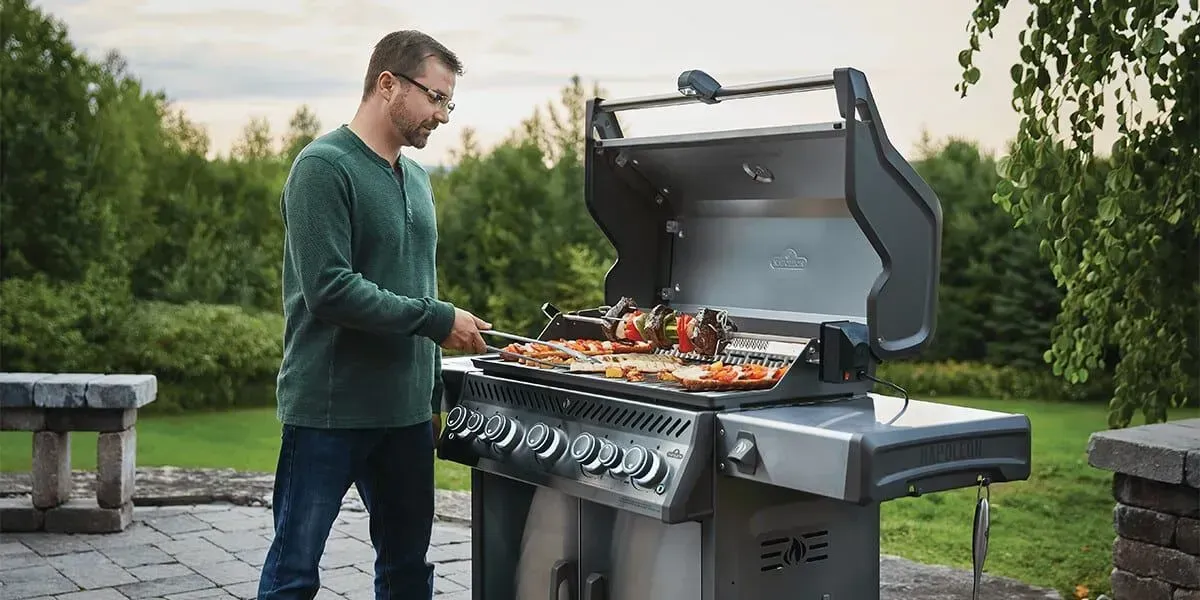 A man grilling food outdoors on a large stainless steel barbecue.