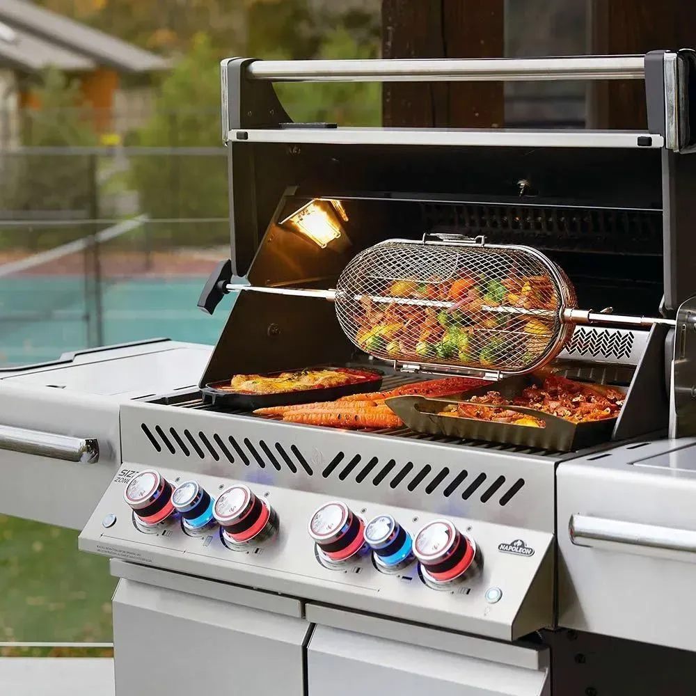 Grill with rotisserie basket and food cooking inside, stainless steel, outdoors.