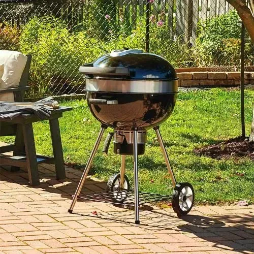 Black charcoal grill on a patio. Chrome legs with wheels; backyard setting with greenery.