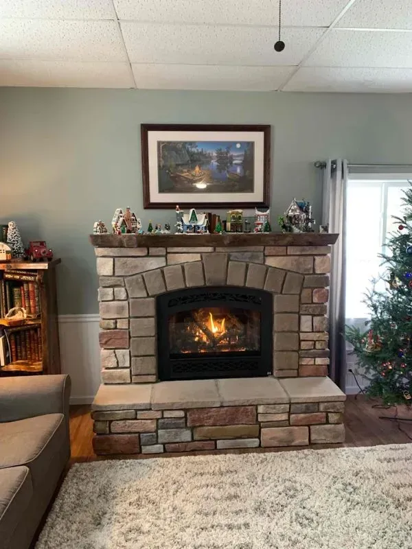 Fireplace with stone facade and wooden mantel, topped with decorative figurines, under framed art.
