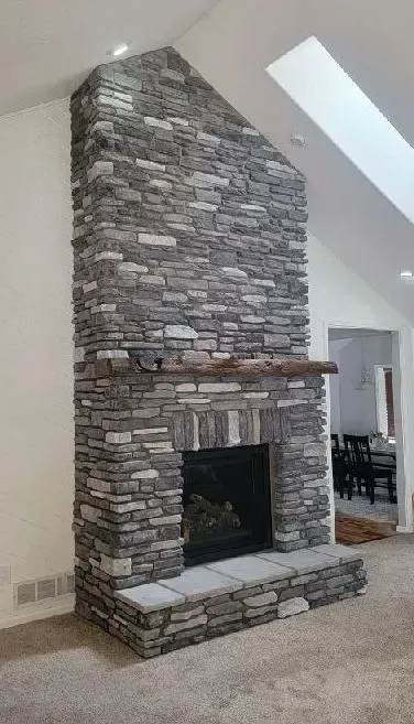 Stone fireplace in a room with neutral walls and carpet, wooden mantel, and a skylight.