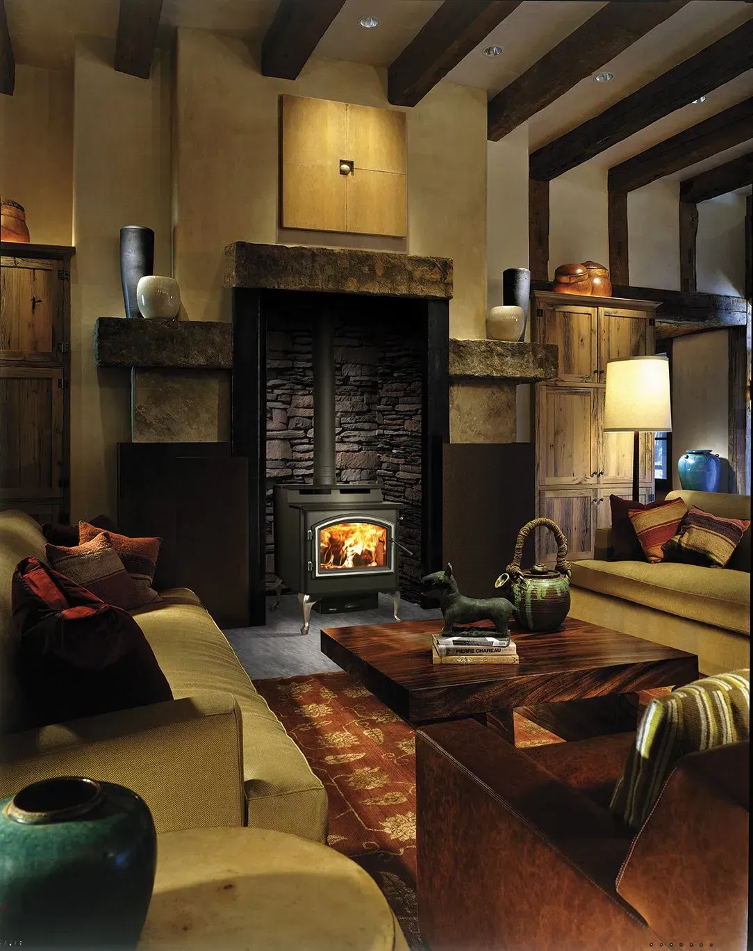 Living room with fireplace, wooden beams, and couches in warm tones.