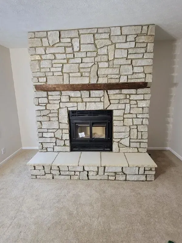 Stone fireplace with dark fireplace insert, wooden beam, and matching stone hearth.