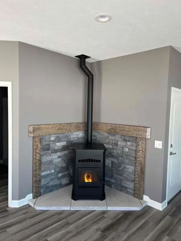 A black pellet stove in a corner, with a gray stone and wood accent wall, gray walls, and a black chimney.