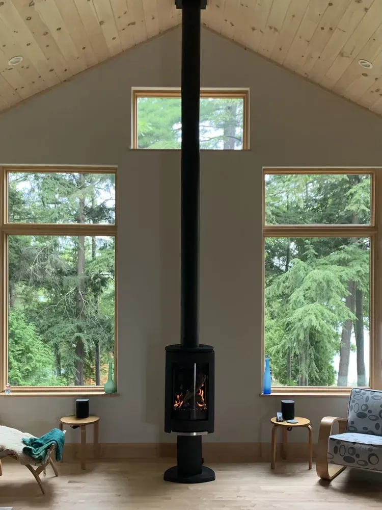 Living room with fireplace, windows overlooking trees; neutral walls and wood floors.