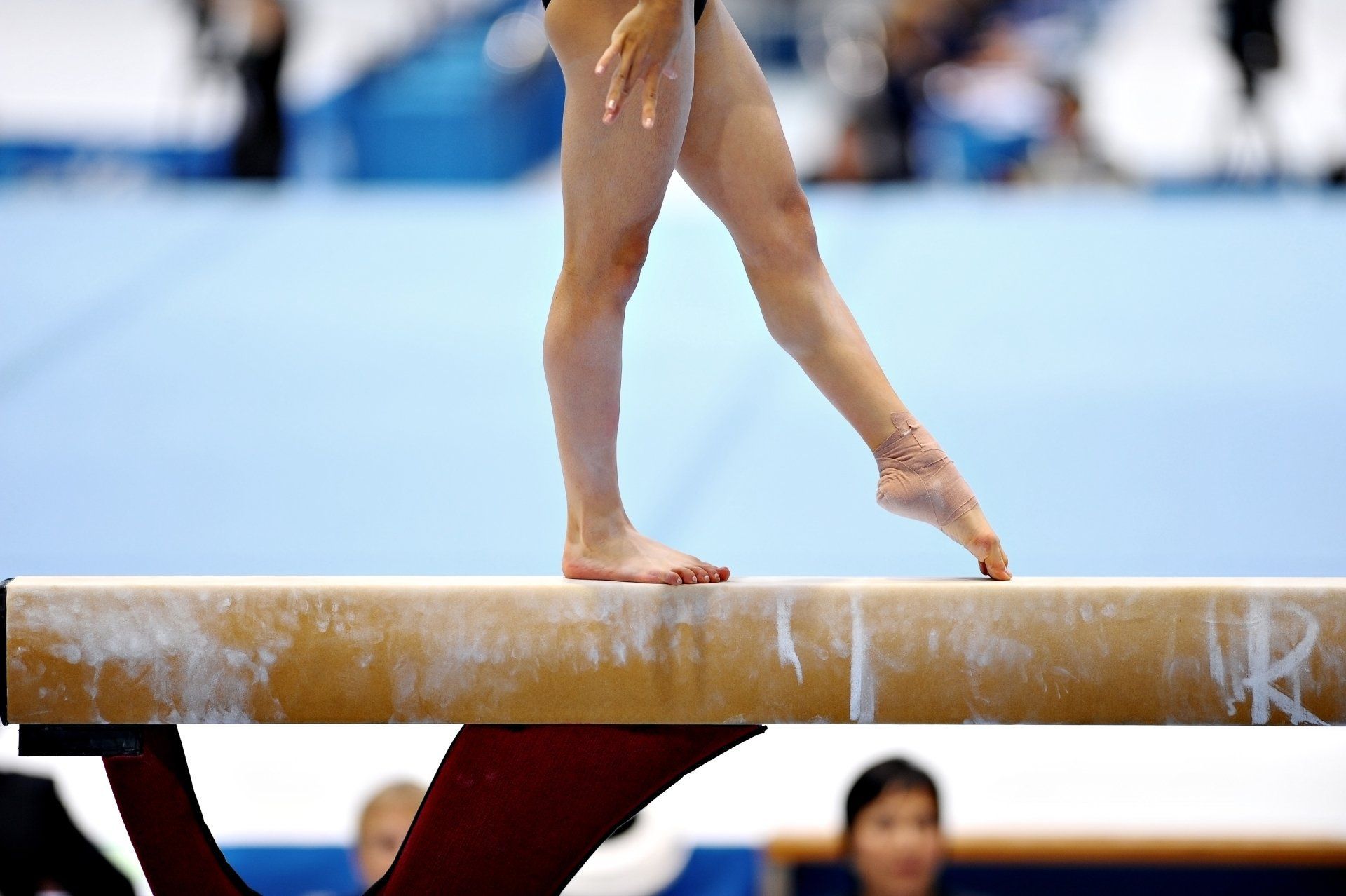 Gymnast balancing on a beam, with one foot pointed on a blue competition floor.