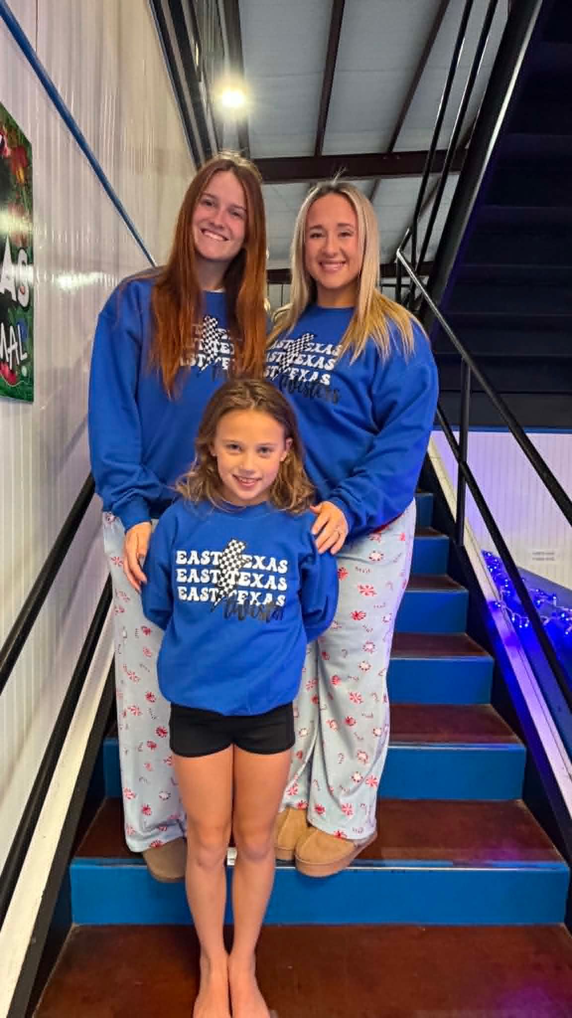 Three smiling people in matching blue sweatshirts standing on indoor stairs