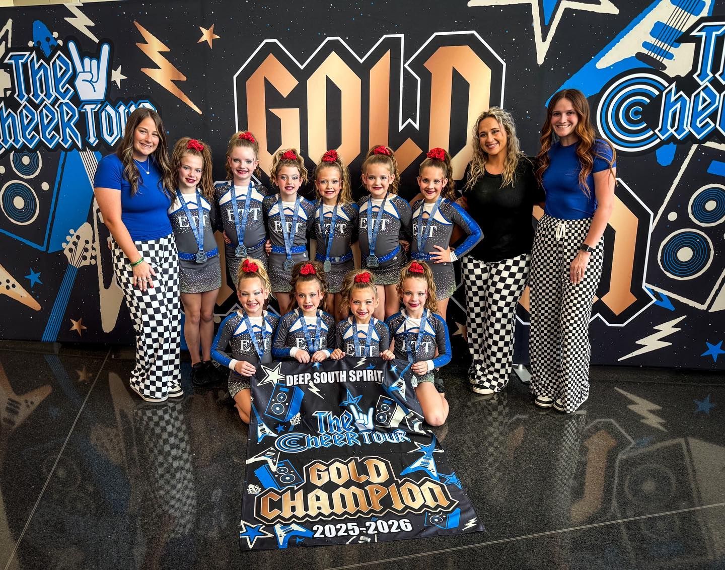 Group of cheerleaders posing in front of a gold championship backdrop with blue-and-black uniforms.