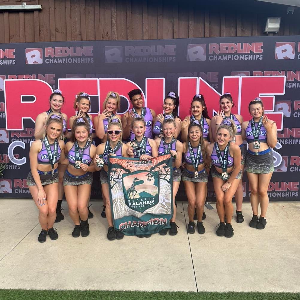 Cheer team posing with a championship banner in front of a Redline Championships backdrop