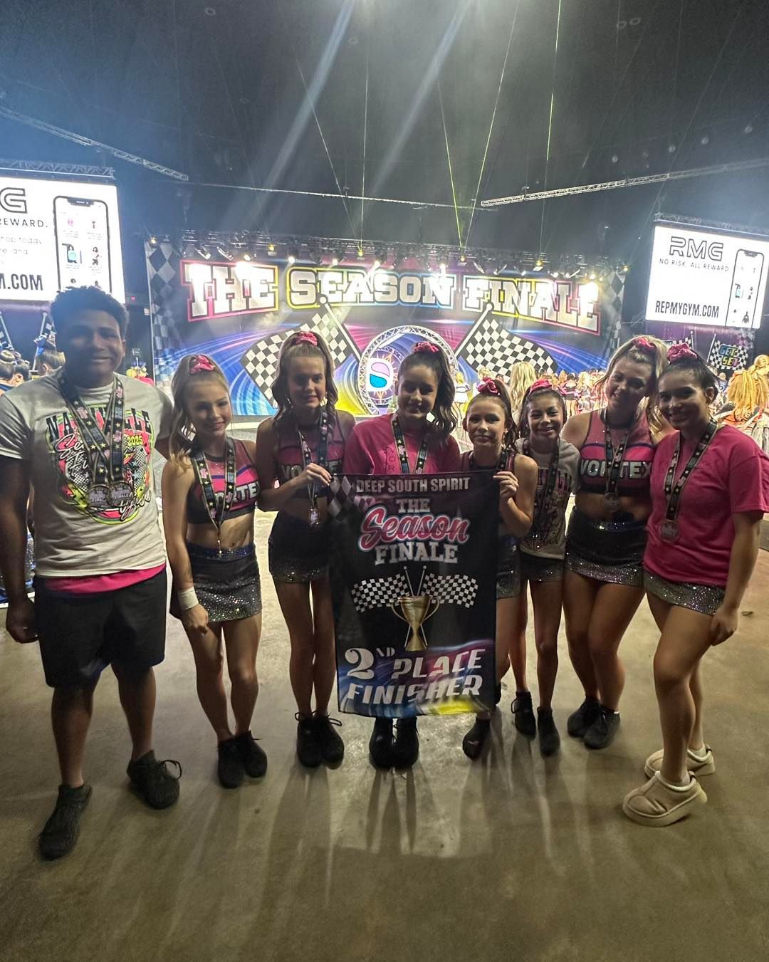 Group posing on a stage with a bright “The Season” sign and colorful lights behind them.