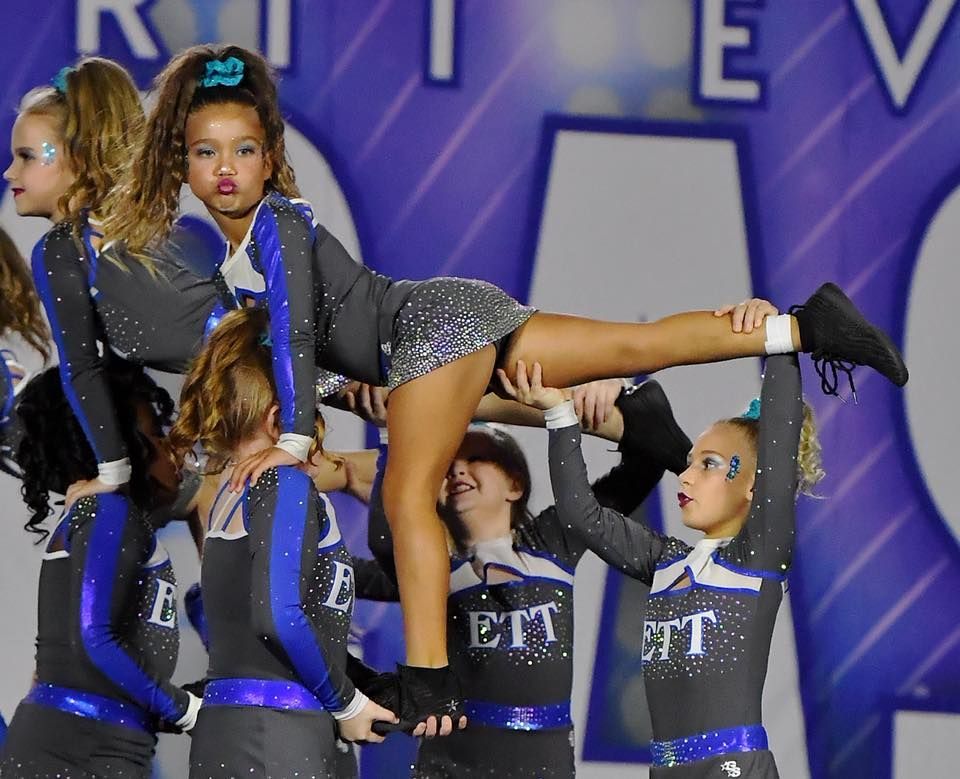 Cheerleaders in black and blue uniforms lift a teammate onstage during a performance