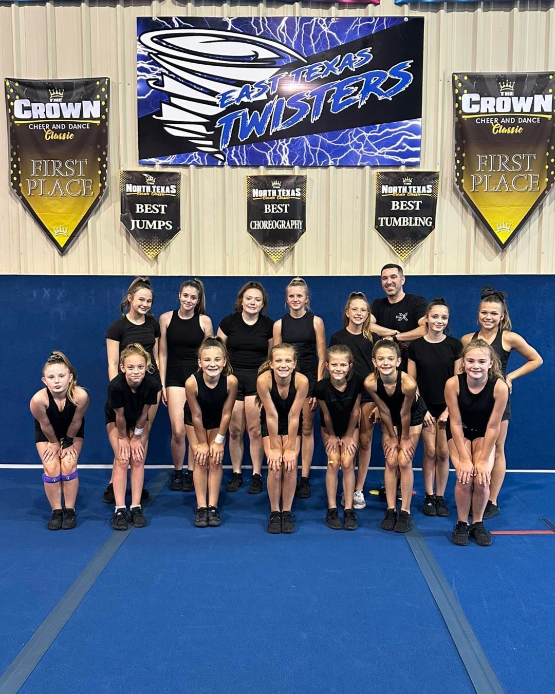 Cheer team posing in a gym with banners and a blue mat background.