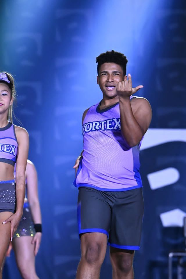 Purple-clad cheerleader pointing forward on a stage with blue lights
