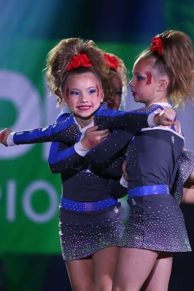 Two young dancers in sparkly blue outfits performing onstage, arms outstretched.