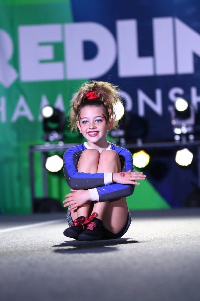 Young gymnast in a blue leotard posing on a lit stage with event backdrop