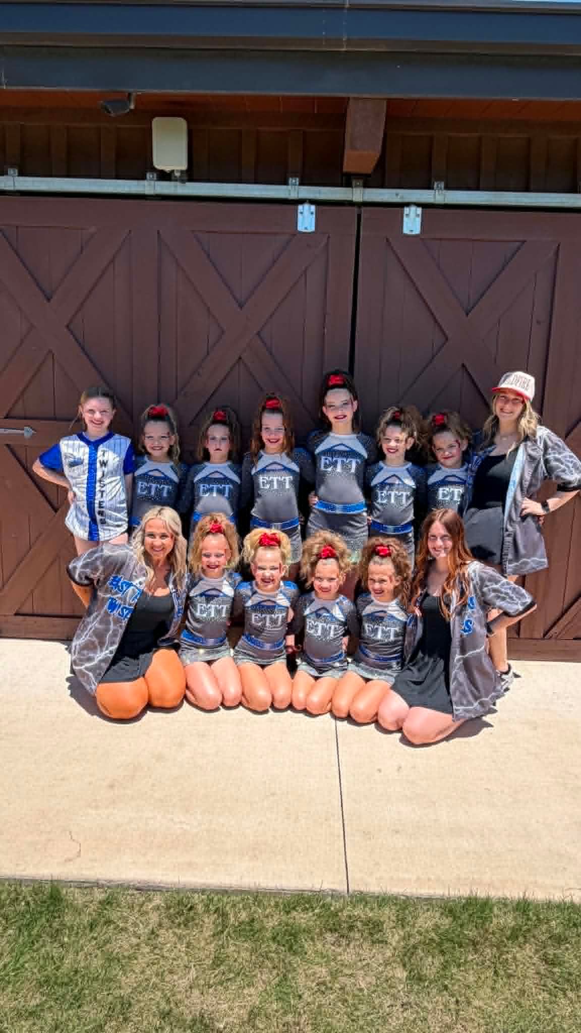 Youth softball team posing in front of a barn door, with orange pumpkins lined across the front row.