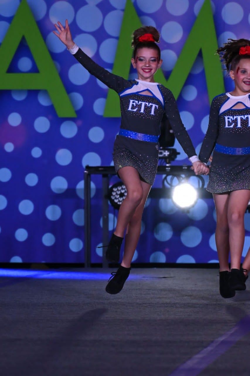 Two dancers in sparkly blue costumes perform on a stage with a blue polka-dot backdrop.