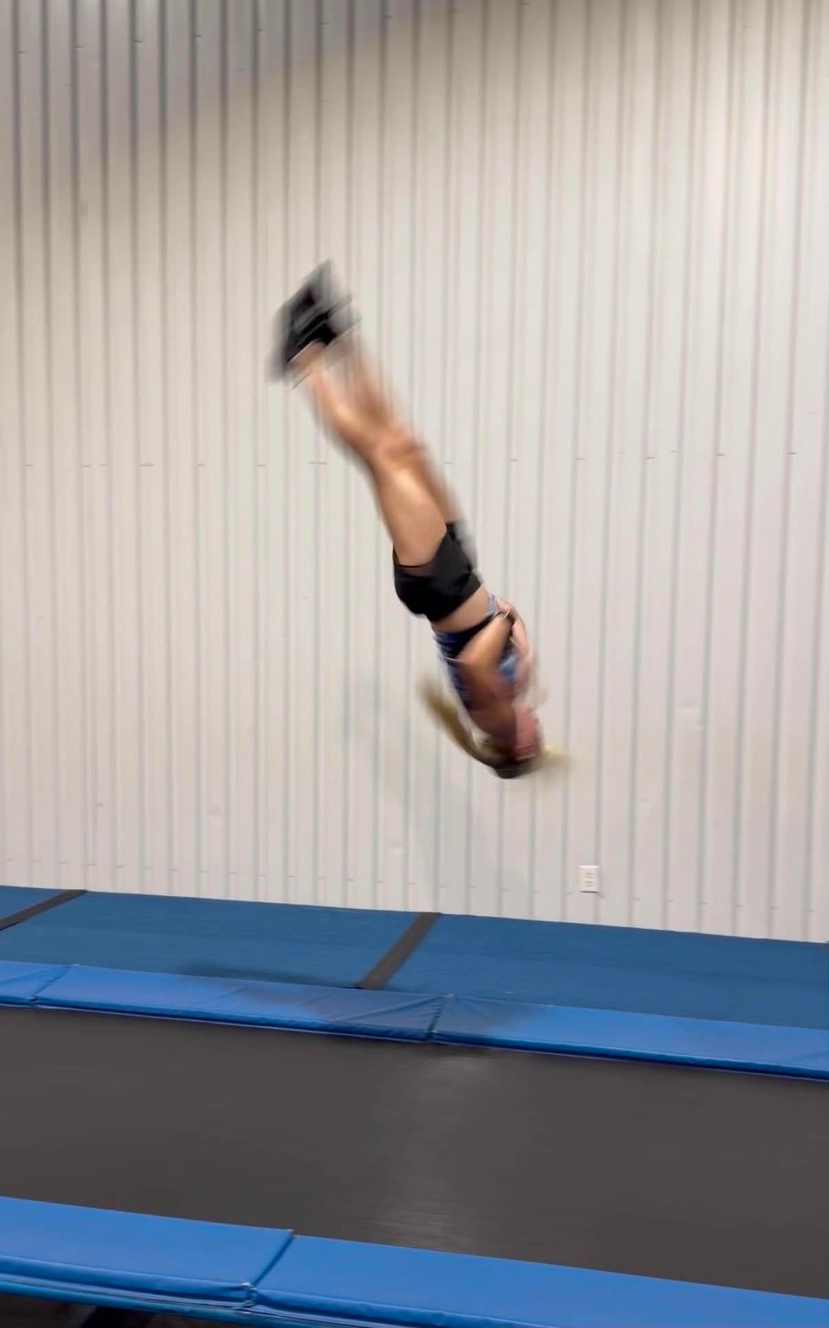 Gymnast mid-backflip above blue mats in a training gym