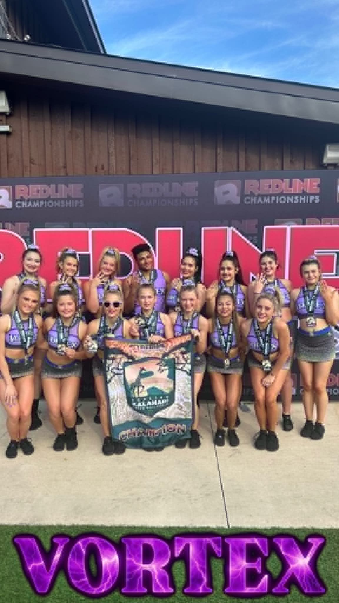 Cheer team posing in front of a Vortex banner, wearing matching black and purple uniforms and holding a team sign
