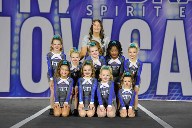 Cheer team posing on a stage with large blue “MONCA” backdrop during Spirit event