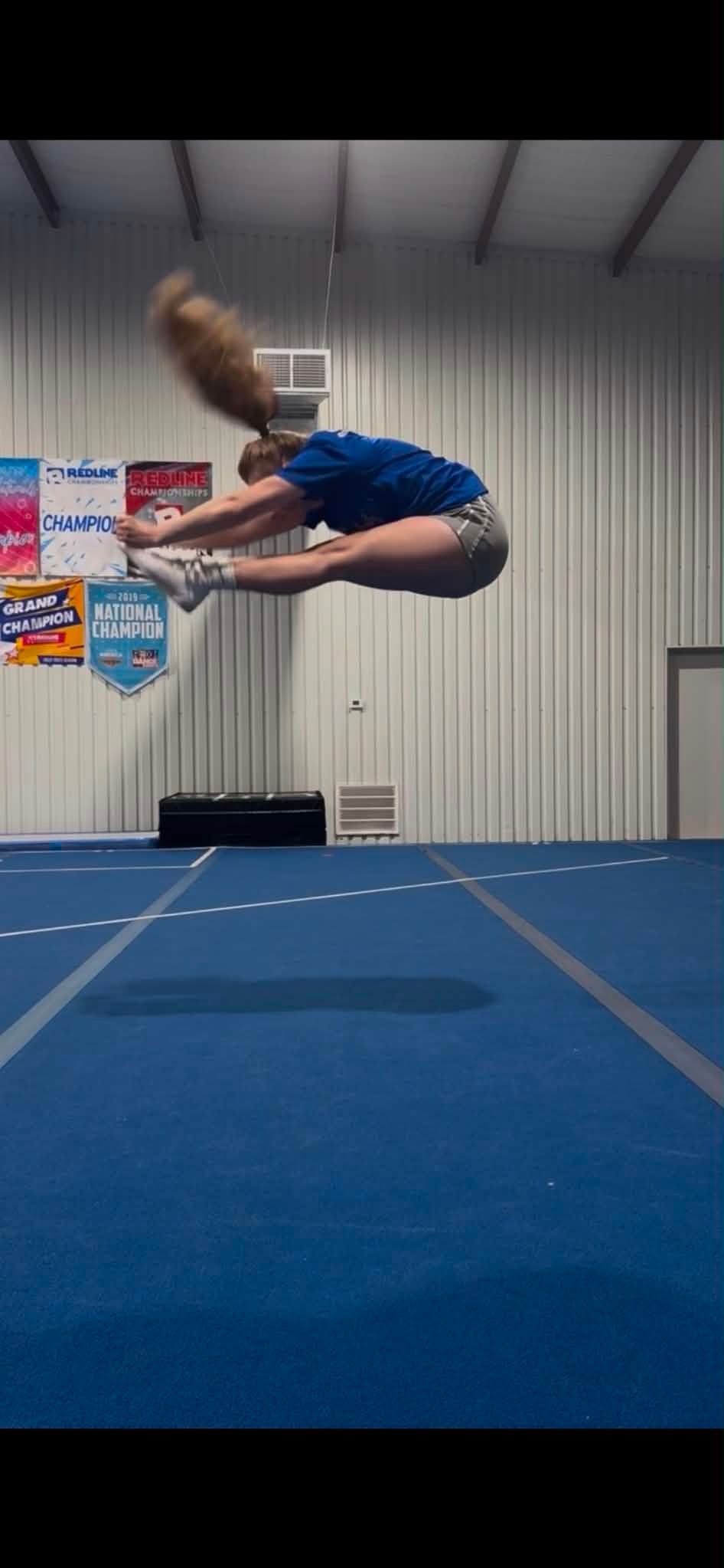 Gymnast mid-backflip above a blue mat in an indoor training gym