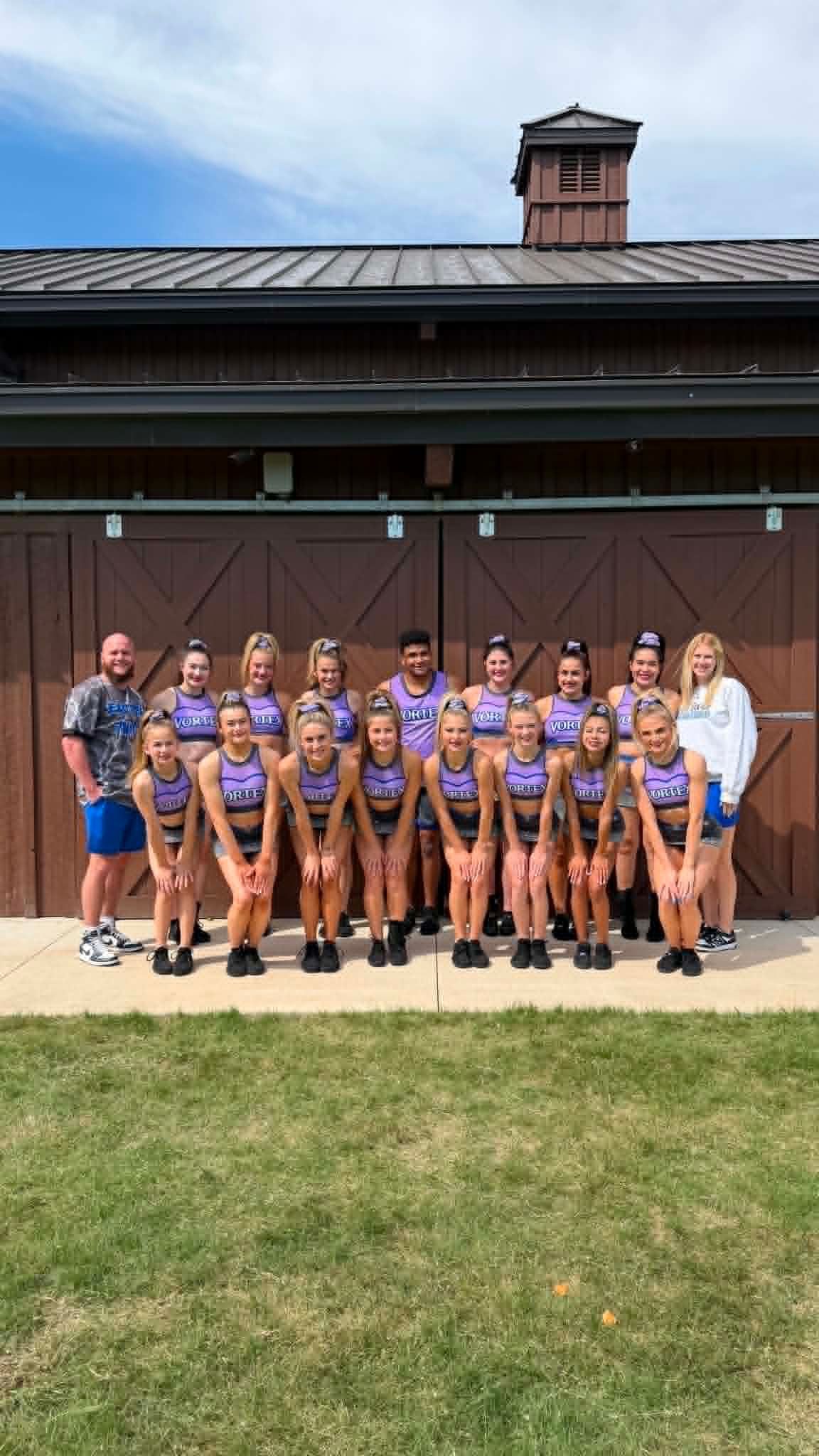 Group of athletes in matching uniforms posing with coaches outside a building, holding a team portrait.