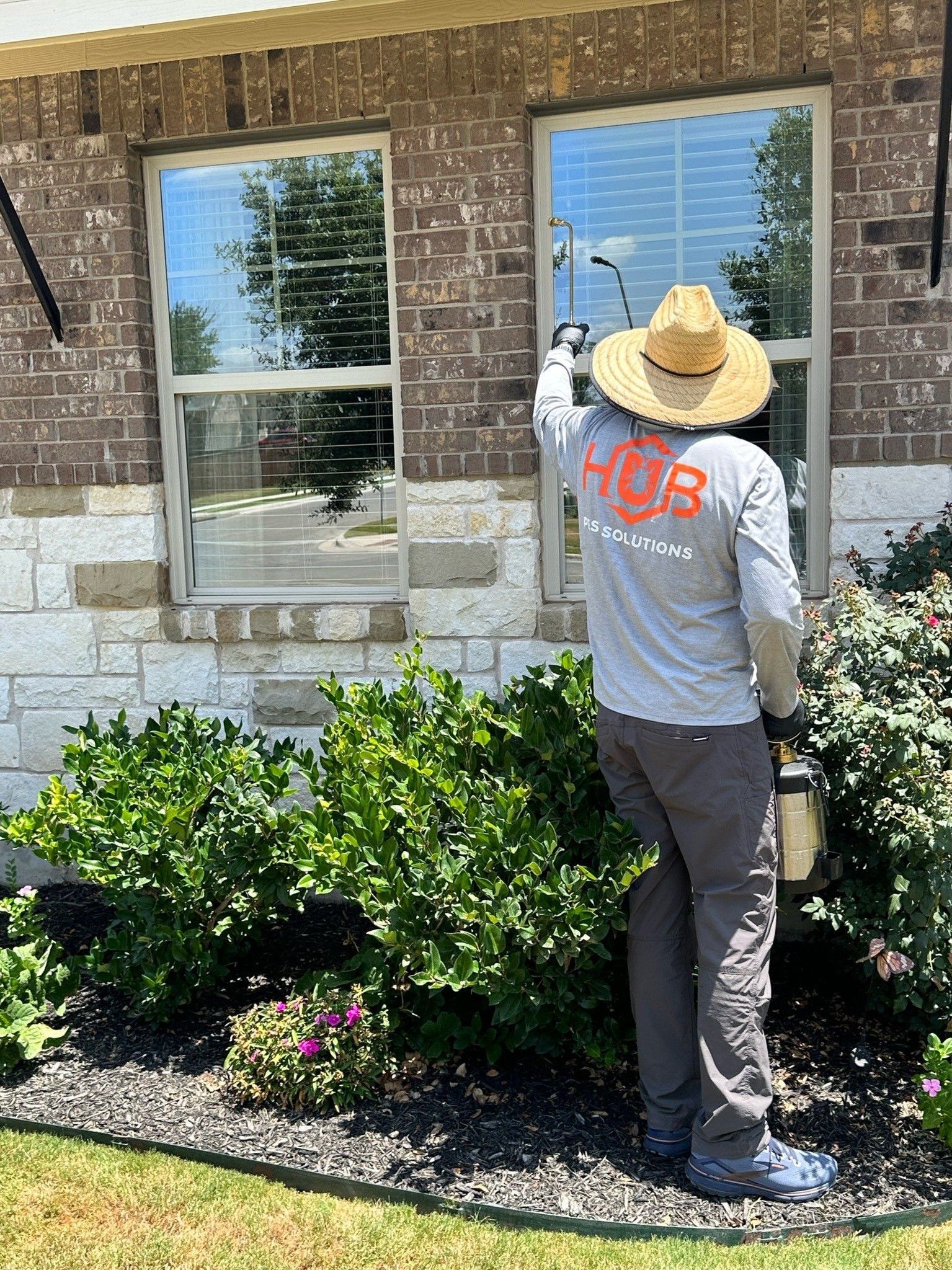 Person washing a window on a brick house. Wearing hat and shirt with 