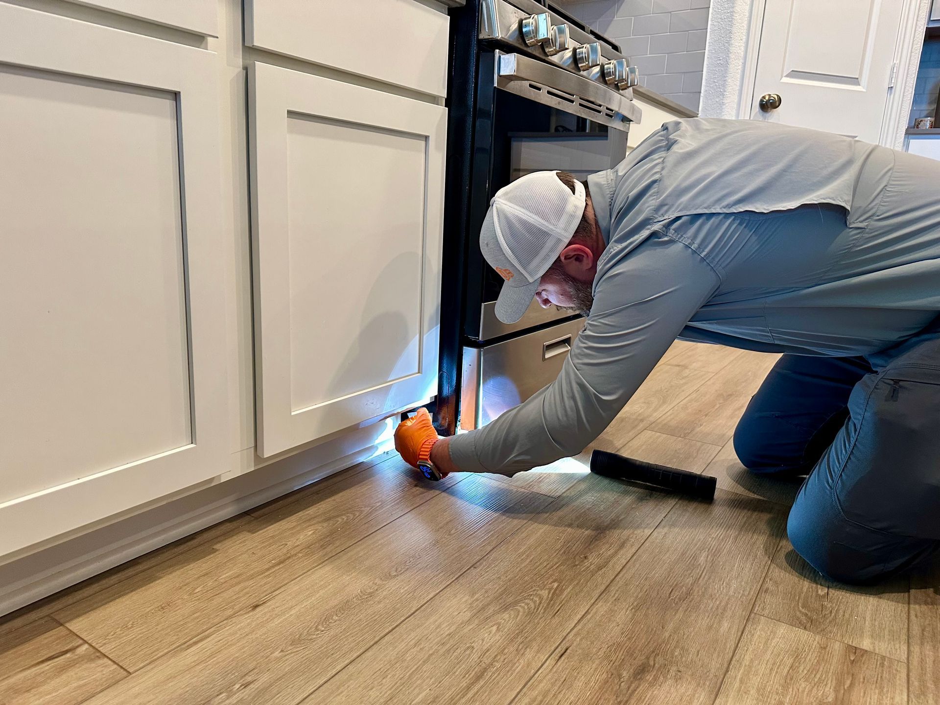 Man inspecting under kitchen cabinets with a flashlight.
